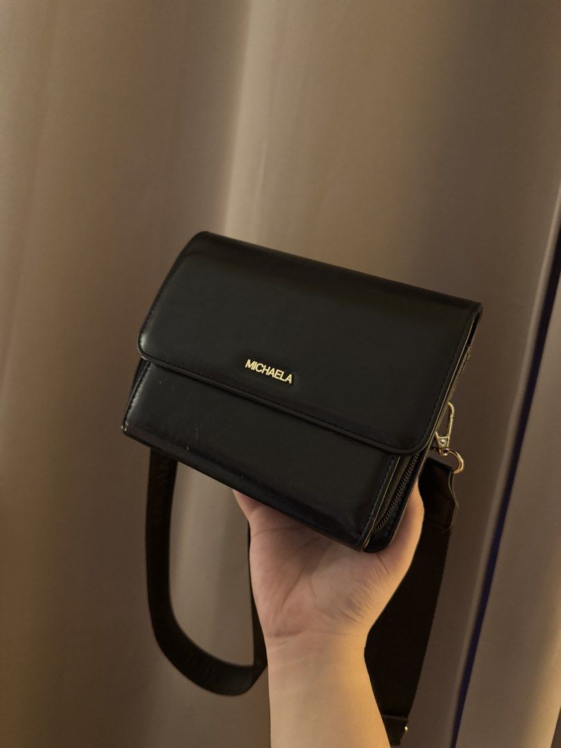 MICHAELA Black Crossbody Bag with Adjustable Strap (Category: Cross-body Bags) located in Mandaluyong City. Submitted by k_closet00 (Listing ID 1470454132, Image 1). Description: - Brand: MICHAELA - Color: Classic Black - Style: Sleek crossbody bag with flap closure and gold lettering logo - Strap: Adjustable fabric shoulder strap - Interior: Clean fabric lining with printed branding, multiple compartments, and zippered sections - In good conditi