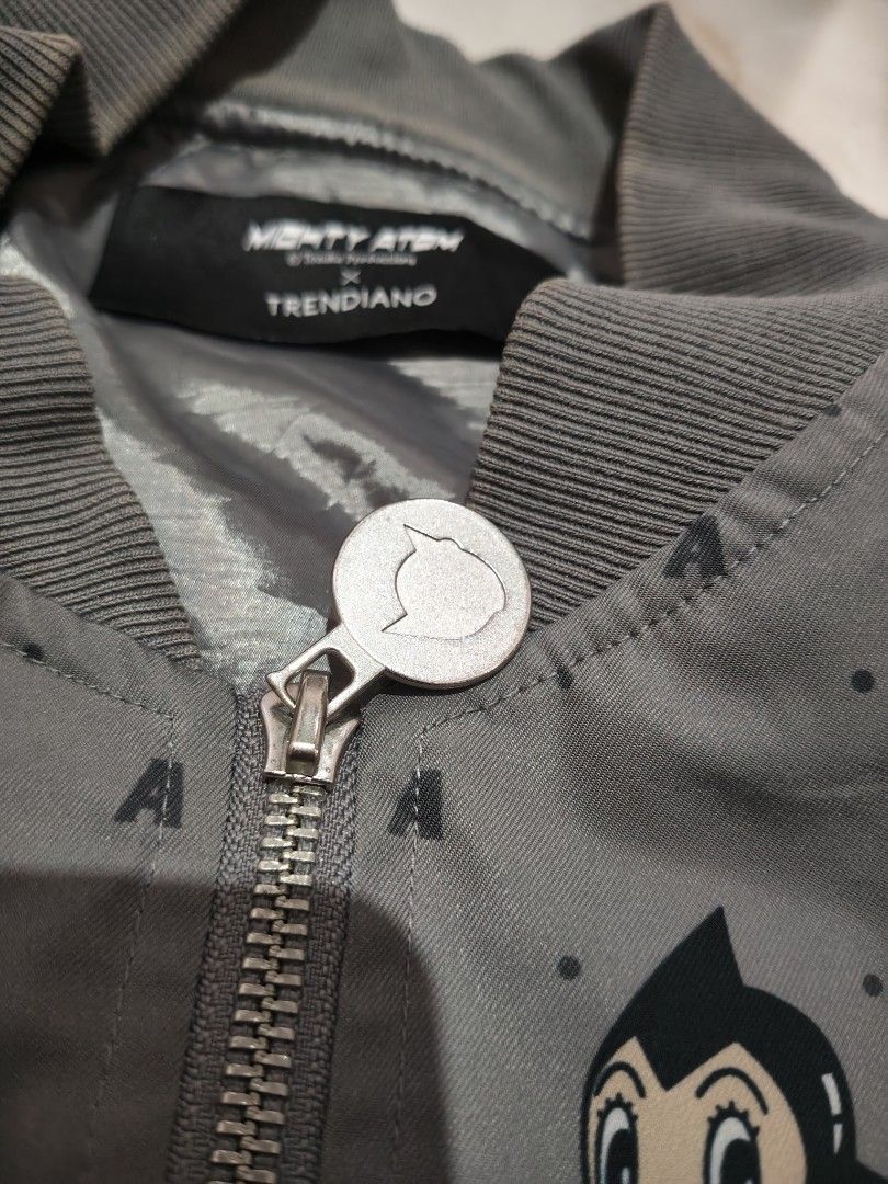 Mighty Atom x Trendiano Astro Boy Bomber Jacket (Category: Coats, Jackets and Outerwear) located in Rizal, Mindoro Occidental. Submitted by finding_ukaygems5103 (Listing ID 1470528841, Image 3). Description: - Brand: Mighty Atom x Trendiano - Color: Dark grey - Design: All-over Astro Boy face graphic print with 'A' letter accents - Closure: Full zip with custom Astro Boy zipper pull - Details: Multiple front and sleeve utility pockets with D-ring