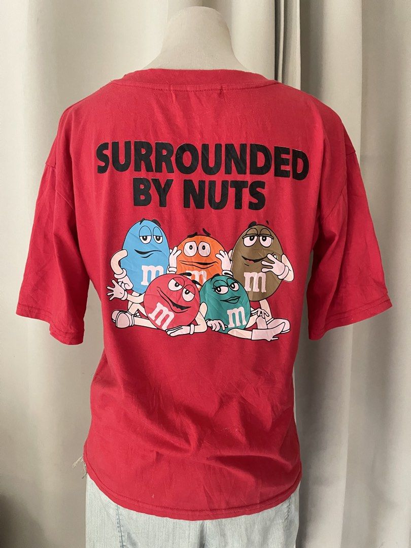 M&M's Mix-Ups Surrounded By Nuts Red Tee (Category: Shirts) located in Cainta. Submitted by zlove111 (Listing ID 1470456428, Image 2). Description: - Color: Bright red - Fit: Relaxed fit with a classic crew neck - Front Detail: Small pink Mix-ups oval logo on the left chest - Back Detail: Large M&M characters graphic with 'Surrounded by Nuts' text - Style: Fun vintage candy merch up to large 21".