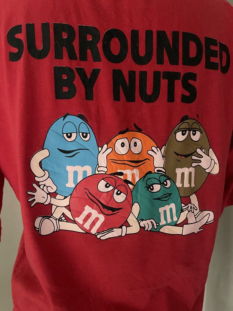 M&M's Mix-Ups Surrounded By Nuts Red Tee (Category: Shirts) located in Cainta. Submitted by zlove111 (Listing ID 1470456428, Image 1). Description: - Color: Bright red - Fit: Relaxed fit with a classic crew neck - Front Detail: Small pink Mix-ups oval logo on the left chest - Back Detail: Large M&M characters graphic with 'Surrounded by Nuts' text - Style: Fun vintage candy merch up to large 21".