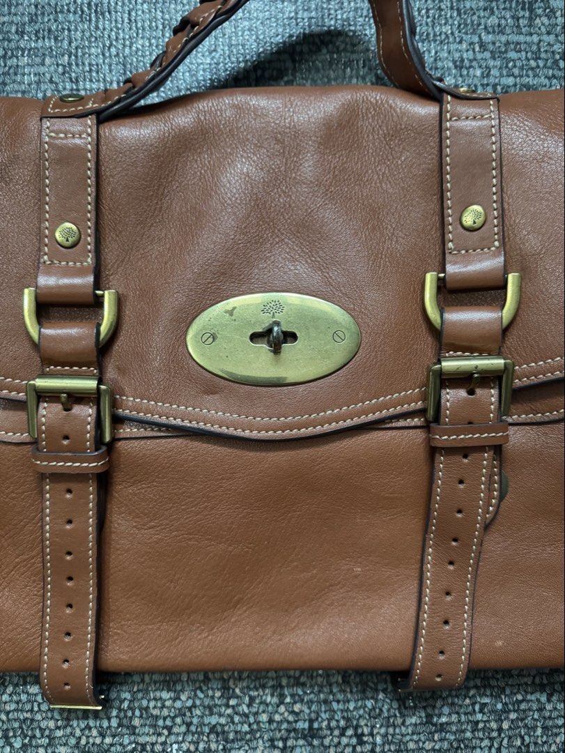 Mulberry Brown Leather Satchel Handbag (Category: Luxury Bags & Wallets) located in Quezon City. Submitted by candyclosetph (Listing ID 1470455697, Image 2). Description: - Authentic Mulberry leather satchel in a rich brown shade - Classic postman lock closure with iconic tree logo and brass-tone hardware - Dual buckle strap front detail with a stylish braided top handle - Olive green fabric interior lining featuring the Mulberry logo pattern wit