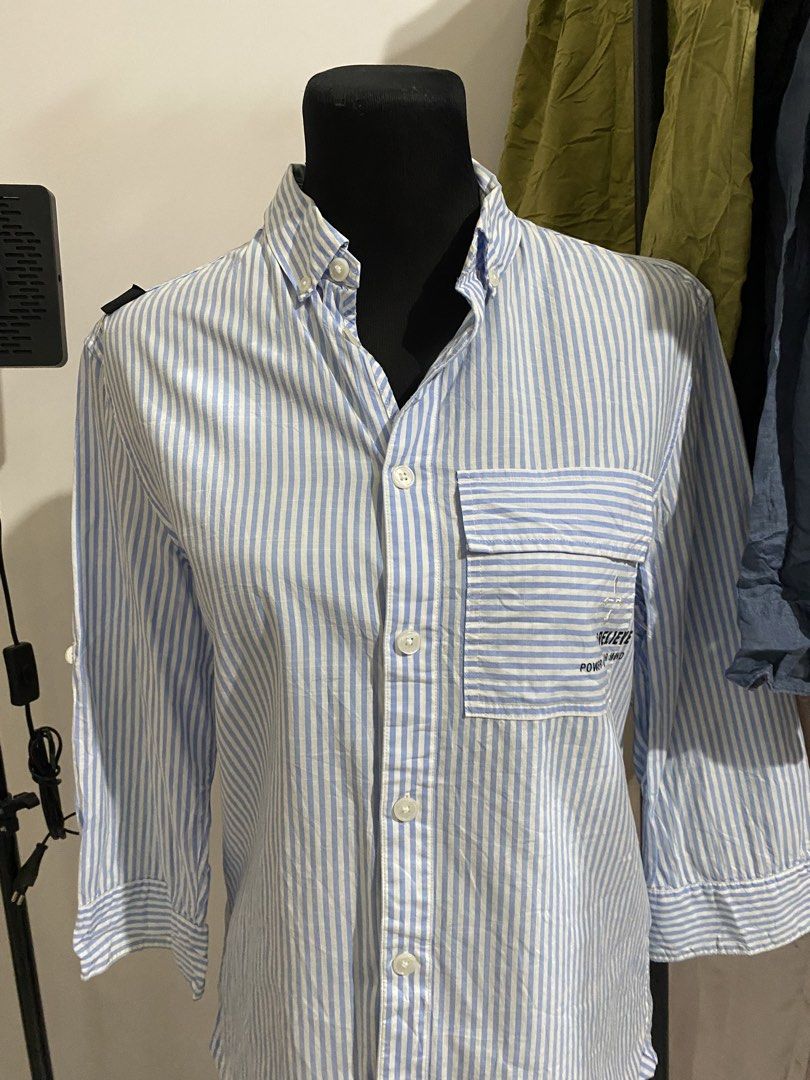 Myth Blue White Striped Button Down Shirt (Category: Tshirts & Polo Shirts ) located in Manila. Submitted by mpt99876 (Listing ID 1470496596, Image 3). Description: - Brand: Myth - Design: Light blue and white vertical stripes - Details: Button collar, chest pocket with 'believe power of your mind' graphic print, and white label tag near the hem - Sleeves: Three-quarter sleeves with convenient button tabs - Style: Versatile casual piece, perfect 
