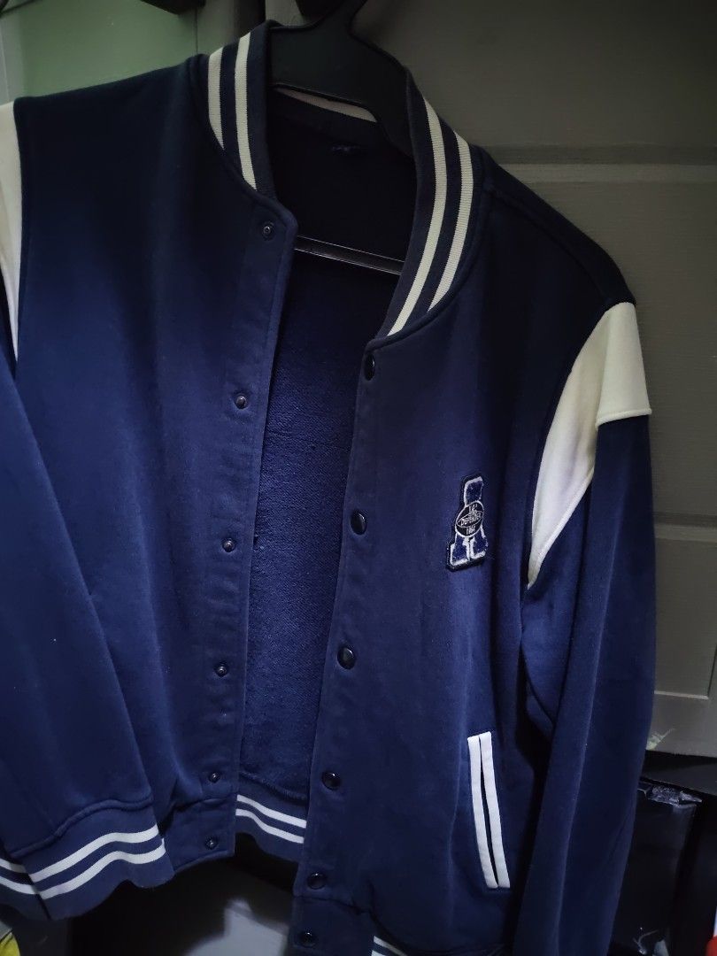 Navy Blue Varsity Jacket with White Details Uniqlo (Category: Coats, Jackets and Outerwear) located in Marikina City. Submitted by hotmom21 (Listing ID 1470425903, Image 1). Description: Dark blue varsity jacket with snap buttons down the front. Cream white accents on the shoulders and striped ribbing along the collar, cuffs, and hem. Small embroidered patch on the left chest. Slanted pockets on both sides. Soft fleece lining inside. Great jacket