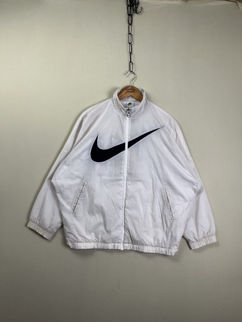 Nike White Windbreaker Jacket Oversized Swoosh (Category: Coats, Jackets and Outerwear) located in Malaybalay. Submitted by toffee_s_thrift0.1 (Listing ID 1470517663, Image 2). Description: - Brand: Nike - Style: Windbreaker with large black swoosh on front, full zip closure, and side pockets - Color: White with black branding - Size: Tagged XS, but fits like a Large (Actual measurements: Width 24.5" x Length 27") - Materials: 100% nylon body, 10