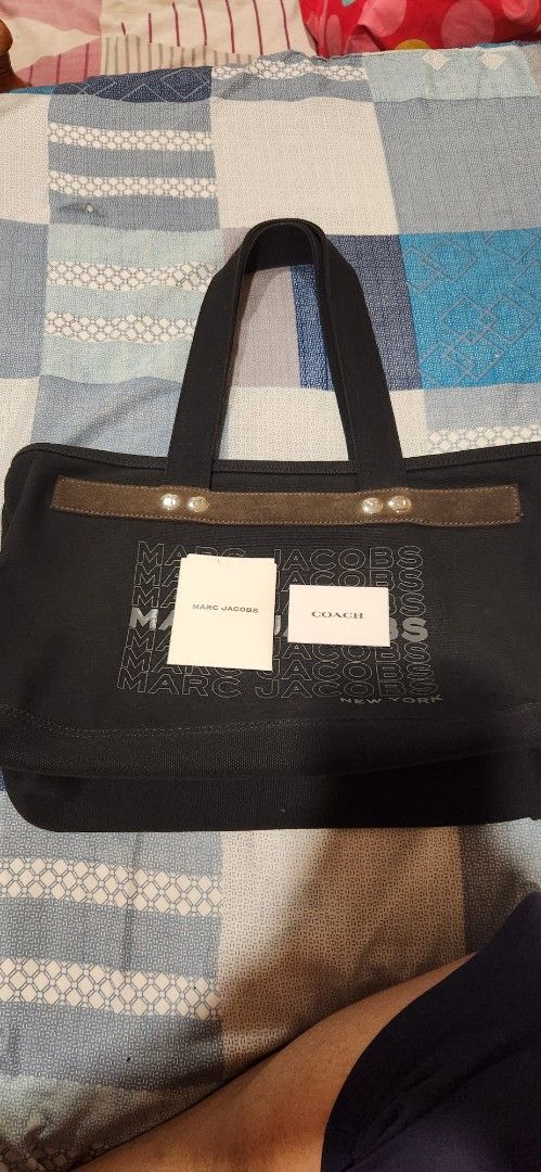Original Marc Jacobs Black Canvas Tote Bag (Category: Tote Bags) located in Marikina City. Submitted by kath_08 (Listing ID 1470351194, Image 2). Description: - Brand: Marc Jacobs - Material: Durable black canvas with dark suede accent trim - Design: Bold stacked lettering print across the front - Closure: Secure top zipper with metallic snap buttons - Interior: Spacious black fabric lining with an open slip pocket - Inclusions: Comes with two wh
