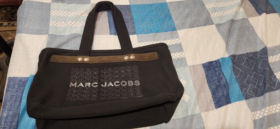Original Marc Jacobs Black Canvas Tote Bag (Category: Tote Bags) located in Marikina City. Submitted by kath_08 (Listing ID 1470351194, Image 1). Description: - Brand: Marc Jacobs - Material: Durable black canvas with dark suede accent trim - Design: Bold stacked lettering print across the front - Closure: Secure top zipper with metallic snap buttons - Interior: Spacious black fabric lining with an open slip pocket - Inclusions: Comes with two wh