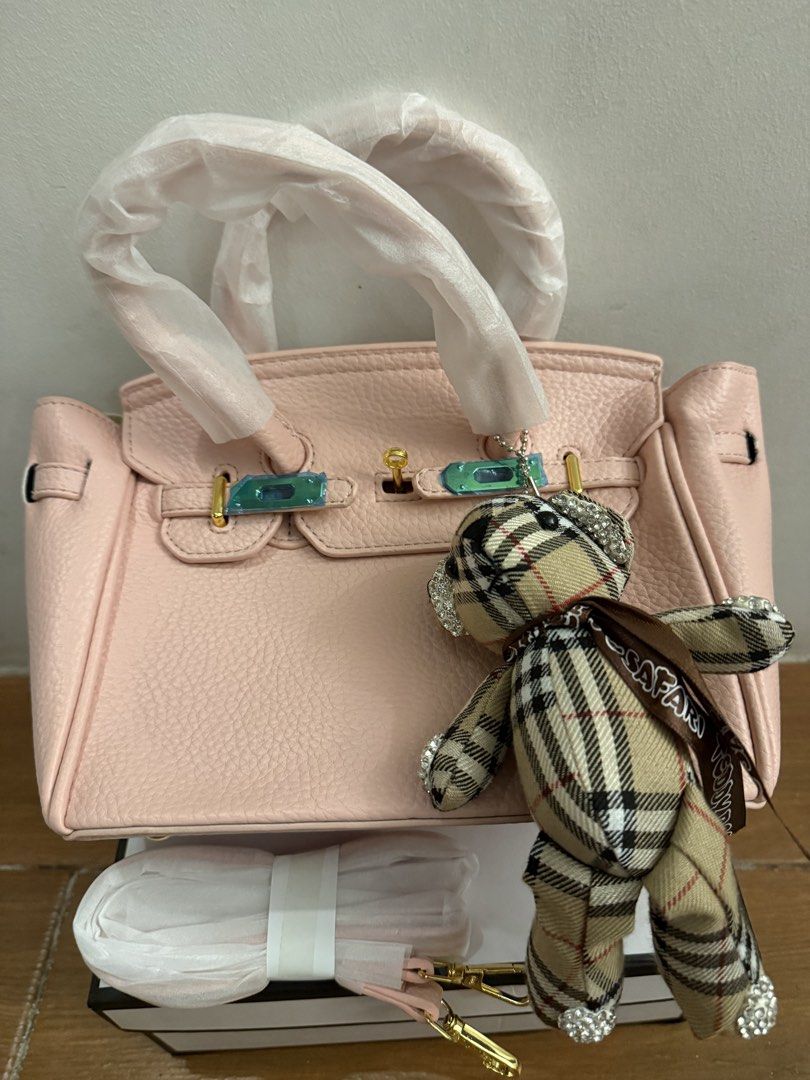 Pink handbag with teddy bear charm & box (Category: Shoulder Bags) located in Bulacan. Submitted by emjay_17 (Listing ID 1470436975, Image 3). Description: - Color: Pink with pebble texture - Hardware: Gold-tone (protective plastic still on metal straps) - Features: Protective bottom feet, matching shoulder strap included, cute plaid teddy bear charm with rhinestones - Packaging: Comes with white box - Condition: Brand new.