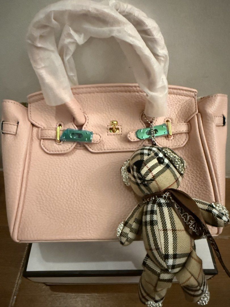 Pink handbag with teddy bear charm & box (Category: Shoulder Bags) located in Bulacan. Submitted by emjay_17 (Listing ID 1470436975, Image 2). Description: - Color: Pink with pebble texture - Hardware: Gold-tone (protective plastic still on metal straps) - Features: Protective bottom feet, matching shoulder strap included, cute plaid teddy bear charm with rhinestones - Packaging: Comes with white box - Condition: Brand new.