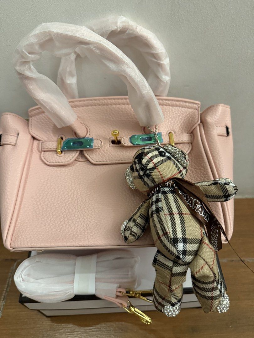 Pink handbag with teddy bear charm & box (Category: Shoulder Bags) located in Bulacan. Submitted by emjay_17 (Listing ID 1470436975, Image 1). Description: - Color: Pink with pebble texture - Hardware: Gold-tone (protective plastic still on metal straps) - Features: Protective bottom feet, matching shoulder strap included, cute plaid teddy bear charm with rhinestones - Packaging: Comes with white box - Condition: Brand new.