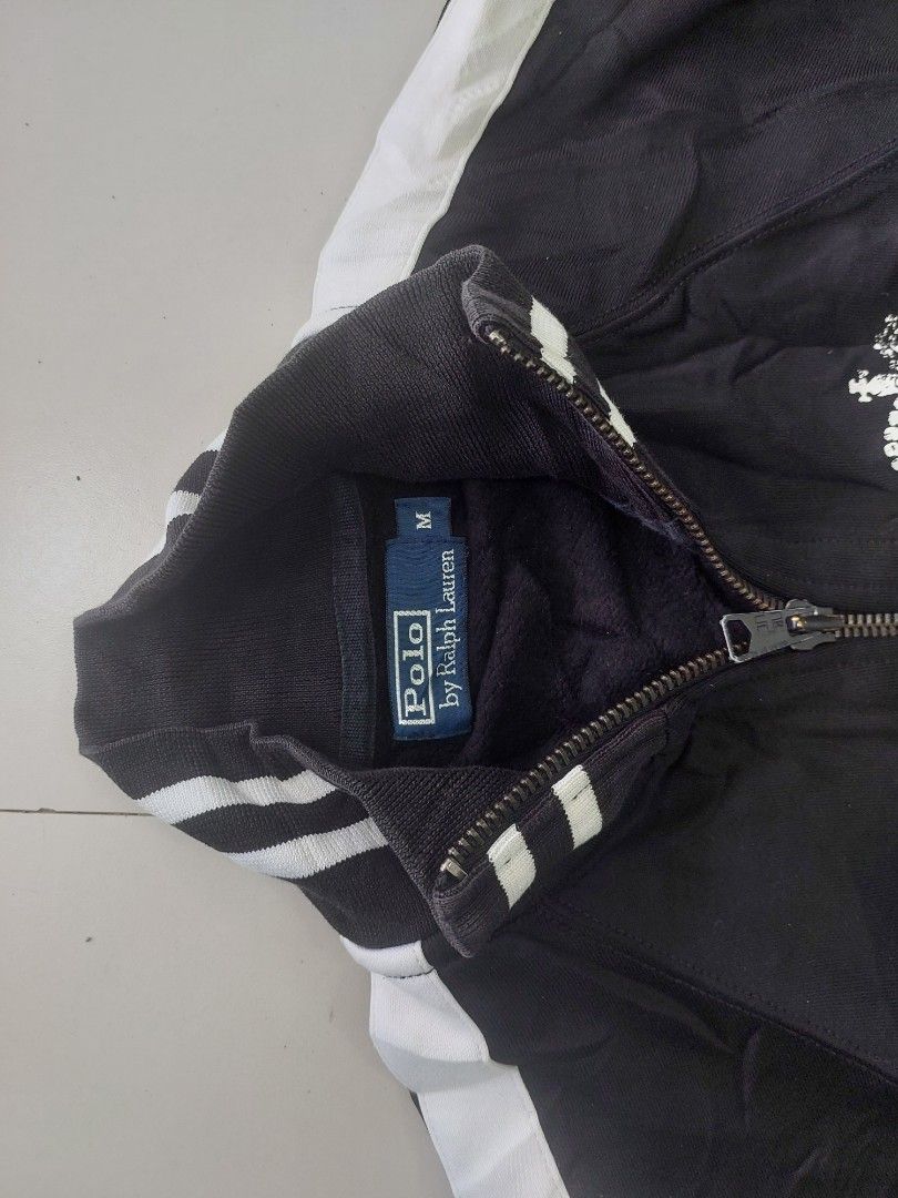 Polo Ralph Lauren Black Track Jacket Size M (Category: Coats, Jackets and Outerwear) located in Caloocan City. Submitted by shikiibun (Listing ID 1470490294, Image 2). Description: - Brand: Polo Ralph Lauren - Color: Black with white side stripes and details - Size: M - Material: 74% nylon, 26% cotton blend - Design: Full zip closure, ribbed collar, cuffs, and hem - Features: Two front pockets and a large crown graphic print on the front.