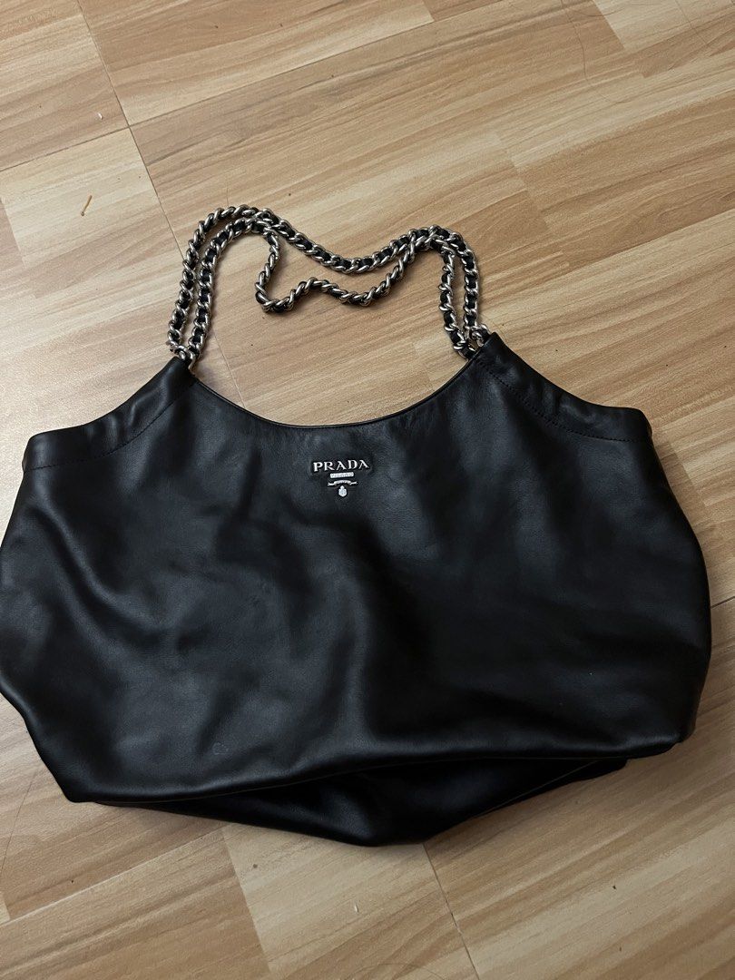 Prada Black Leather Chain Tote Bag (Category: Luxury Bags & Wallets) located in Victorias. Submitted by lan1877 (Listing ID 1470476161, Image 1). Description: - Brand: Prada - Color: Classic Black - Material: Soft, high-quality leather - Hardware: Silver-tone chain straps - Closure: Magnetic main closure with internal zip compartments - Branding: Signature Prada Milano logo plaque on front and interior - Style: Structured yet slouchy tote, perfec