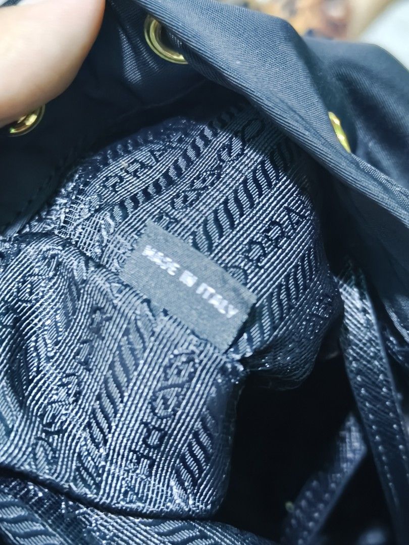 Prada Black Nylon Bucket Bag with Gold Hardware (Category: Luxury Bags & Wallets) located in Davao. Submitted by navil01 (Listing ID 1470489776, Image 3). Description: - Style: Black nylon bucket bag with gold-tone hardware - Branding: Iconic triangle logo plaque on front zipped pocket - Closure & Handling: Drawstring top closure with matching handle - Interior: Lined with Prada logo fabric, includes 'Made in Italy' and factory number tag 24 - De