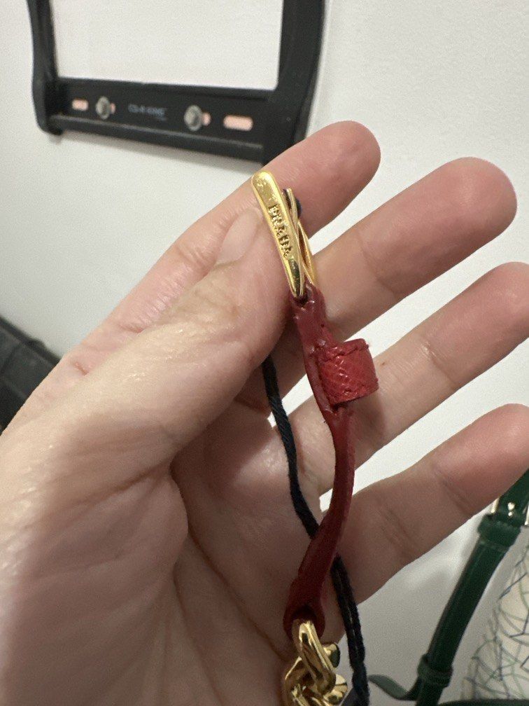 Prada Saffiano Leather Chain Charm Bracelet (Category: Bracelets) located in Malabon City. Submitted by seseche (Listing ID 1470526286, Image 2). Description: Prada Saffiano Leather Chain Charm Bracelet (Model: 1IB263). It is characterized by its red or peony pink crosshatch Saffiano leather strap, a gold-finished chain section, an adjustable buckle closure, and a dangling round charm featuring the engraved Prada logo..