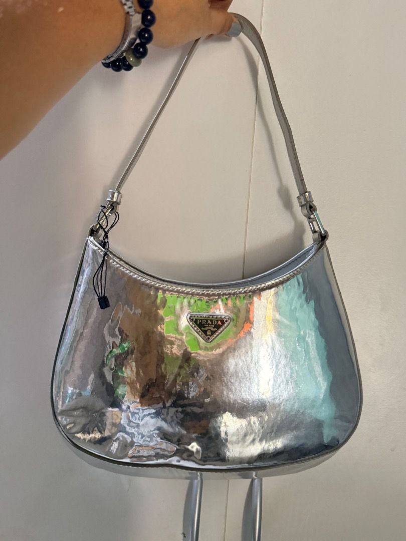 Prada Silver Metallic Shoulder Bag (Category: Luxury Bags & Wallets) located in Manila. Submitted by _outofthecloset. (Listing ID 1470394952, Image 1). Description: - Brand: Prada - Style: Curved hobo shoulder bag with single strap - Color: Metallic silver - Hardware/Logo: Front enamel triangular logo plaque & Prada Milano metal tag - Closure: Magnetic top closure - Interior: Black signature fabric lining with extra slip pocket - Condition: Clean