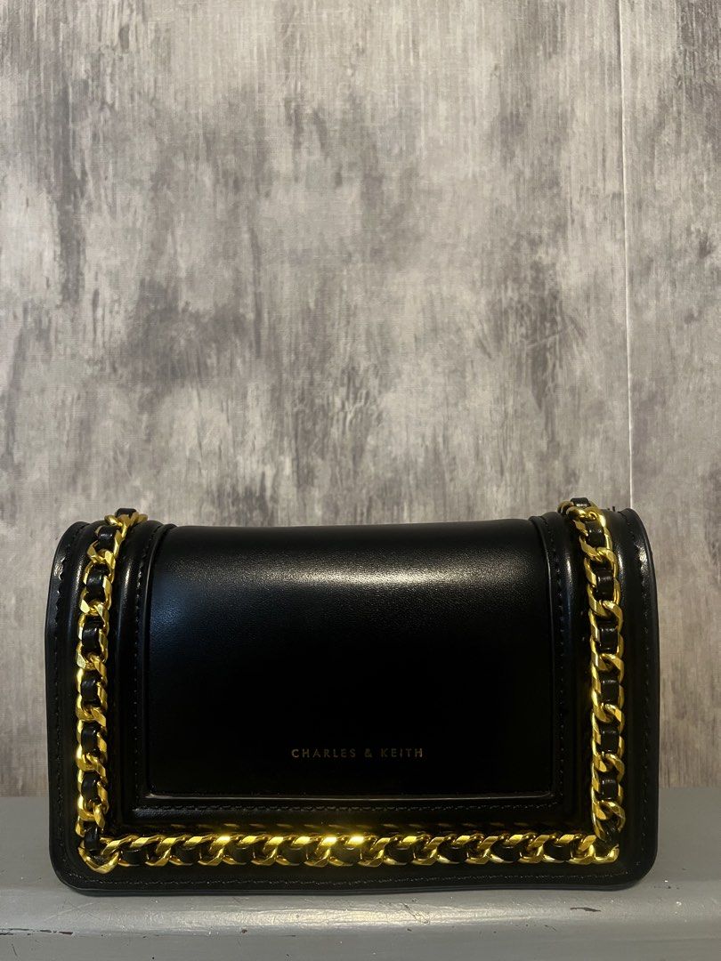 Preloved bags (Category: Cross-body Bags) located in Calamba. Submitted by saiphsavion (Listing ID 1470455448, Image 2). Description: Black Charles & Keith shoulder bag. Structured silhouette with gold-tone hardware. Thick chain straps threaded with black material wrap around the sides. Flap closure on the front with gold lettering branding. Smooth faux leather material. Compact size for daily essentials, evening out, or casual errands..