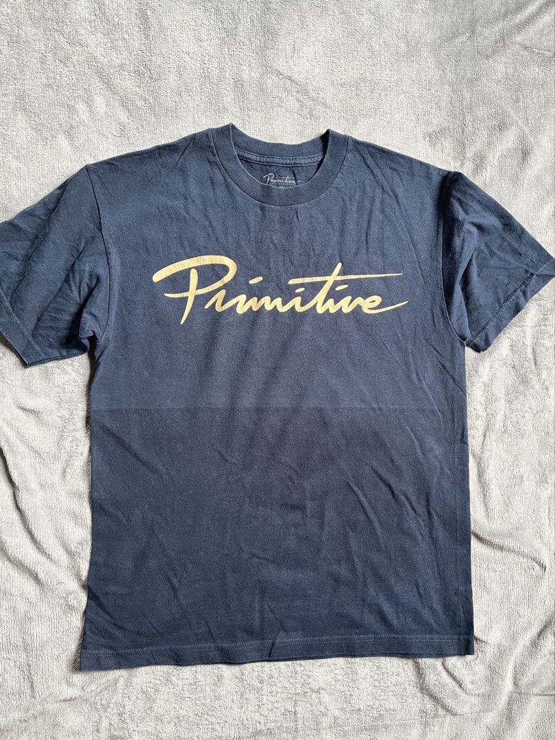 Primitive Skateboarding Graphic T-Shirt (Category: Tshirts & Polo Shirts ) located in Urdaneta. Submitted by m1k3yl (Listing ID 1470392620, Image 1). Description: - Brand: Primitive Skateboarding - Color: Dark navy blue with gold metallic script logo - Size: Medium (Standard Fit) - Material: 100% Cotton - Condition: Good, with minor graphic cracking from wear - Style: Classic streetwear staple, crew neck, short sleeves.