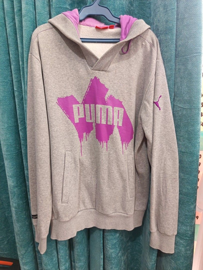 Puma hoodie (Category: Coats, Jackets and Outerwear) located in Cavite. Submitted by vin2za06 (Listing ID 1470384104, Image 2). Description: The image shows a grey PUMA pullover hoodie with a purple and silver brushstroke-style PUMA logo on the front, a V-neck hood lined with purple fabric, and a front kangaroo pocket..