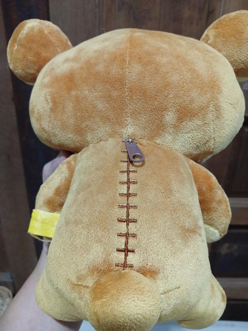 Rilakkuma Bear Plush Toy with Zipper (Category: Plushies & Soft Toys) located in Antipolo. Submitted by u_buy (Listing ID 1470522262, Image 2). Description: Rilakkuma plush toy with white tummy and yellow inner ears. Zipper detail running down the back. Yellow tag attached to the side near the arm. Soft fabric material, about 20 cm in length. Clean surface, no tears or loose threads found..