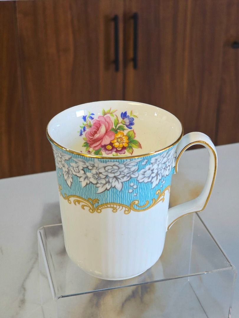 Royal Albert Enchantment Bone China Mug (Category: Coffee & Tea Tableware) located in Compostela. Submitted by curatedcabinetcebu (Listing ID 1470543109, Image 1). Description: - Brand/Pattern: Royal Albert Enchantment - Material: Bone China (Made in England, 1950 vintage) - Design: Turquoise blue and white floral border with luxurious gold trim - Special Feature: Charming rose bouquet cluster on the inside rim - Condition: Classic collectible te