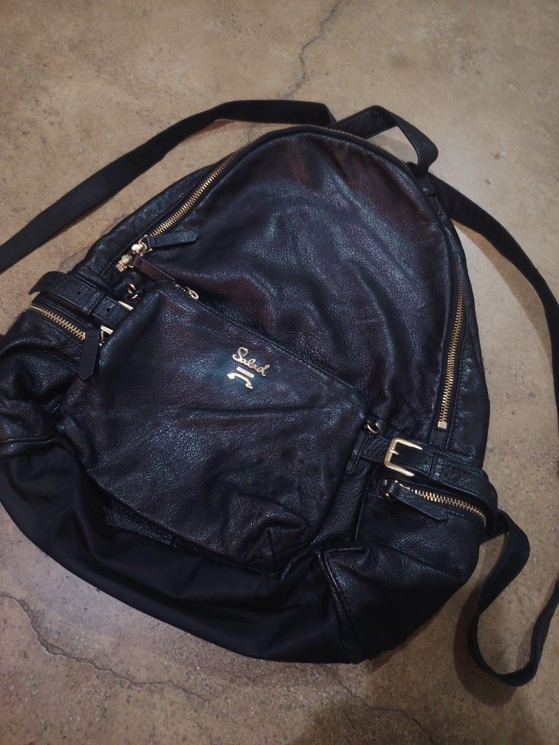 Salad Leather Backpack (Category: Backpacks) located in San Jose del Monte. Submitted by klowiboy (Listing ID 1470349752, Image 1). Description: Black leather backpack from Salad. Gold-tone hardware and zippers throughout. Front pocket with embossed logo plate. Signature patterned interior lining with zip pocket. Buckle strap details on the sides. Professional styling, daily wear ready. Excellent Condition✅️ 999 ONLY.