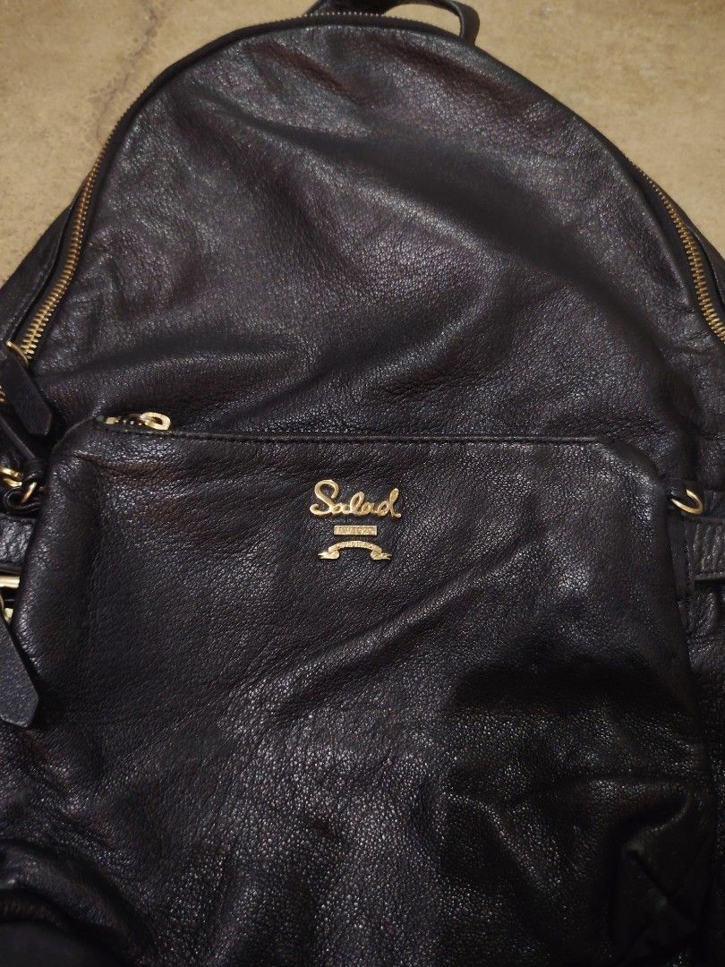 Salad Leather Backpack (Category: Backpacks) located in San Jose del Monte. Submitted by klowiboy (Listing ID 1470349752, Image 2). Description: Black leather backpack from Salad. Gold-tone hardware and zippers throughout. Front pocket with embossed logo plate. Signature patterned interior lining with zip pocket. Buckle strap details on the sides. Professional styling, daily wear ready. Excellent Condition✅️ 999 ONLY.