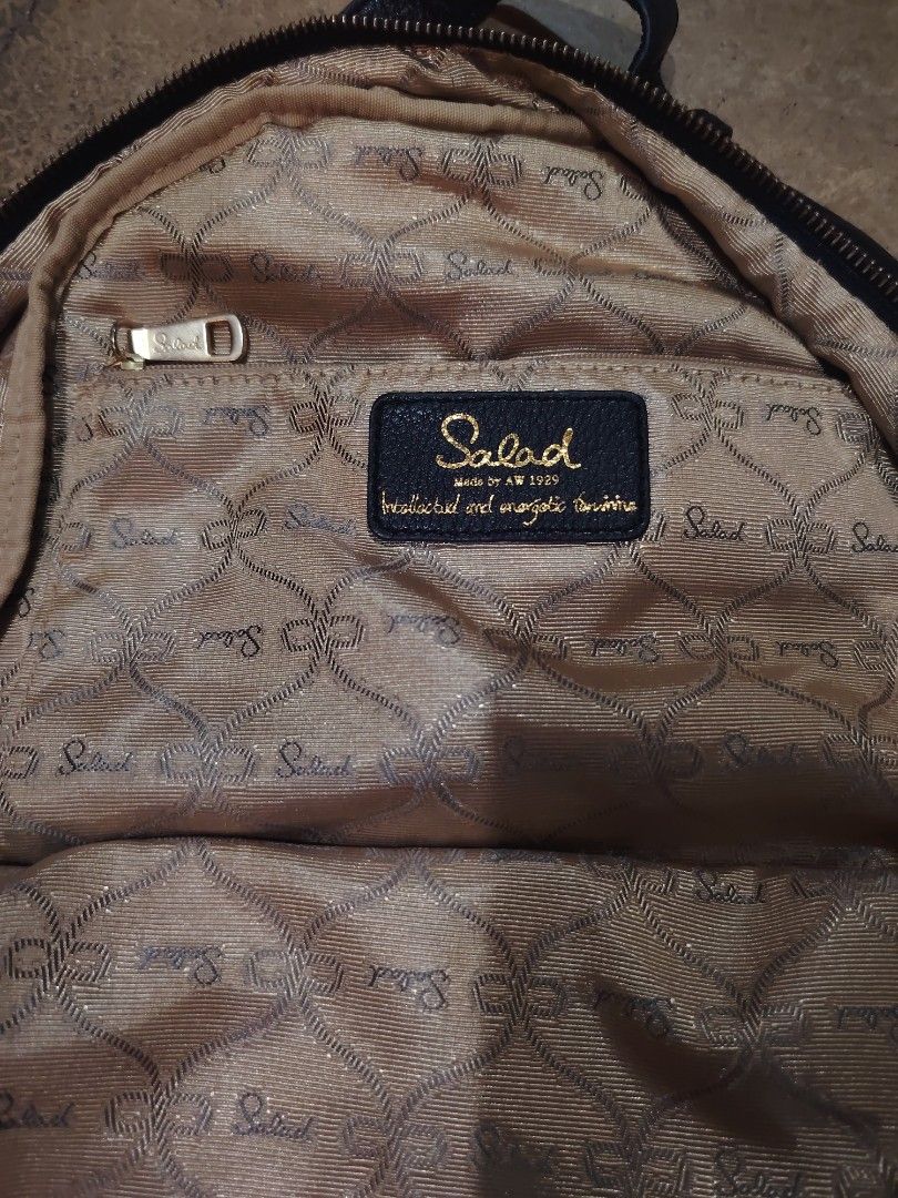 Salad Leather Backpack (Category: Backpacks) located in San Jose del Monte. Submitted by klowiboy (Listing ID 1470349752, Image 3). Description: Black leather backpack from Salad. Gold-tone hardware and zippers throughout. Front pocket with embossed logo plate. Signature patterned interior lining with zip pocket. Buckle strap details on the sides. Professional styling, daily wear ready. Excellent Condition✅️ 999 ONLY.