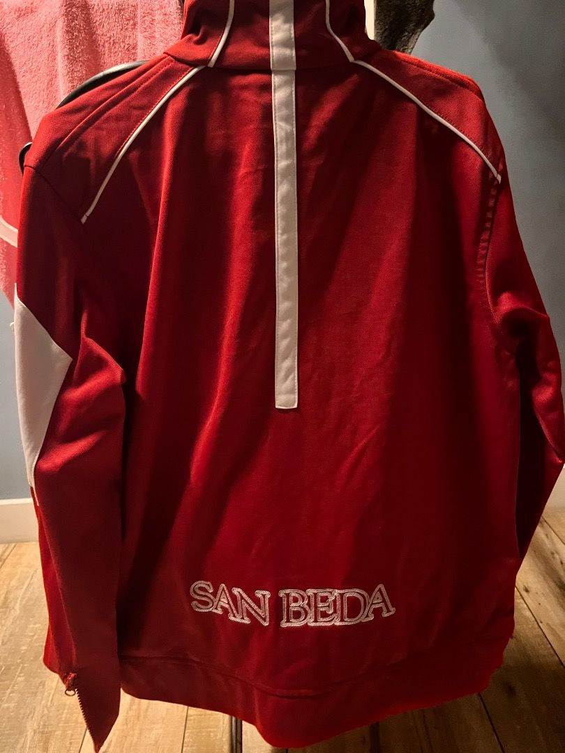 San Beda Red Lions Track Jacket Red White (Category: Coats, Jackets and Outerwear) located in Pasig City. Submitted by vastpenguin.671612 (Listing ID 1470451680, Image 2). Description: - Color: Red with white piping and shoulder panels - Design: Full zip front with stand-up collar and front pockets - Branding: Embroidered San Beda lion crest on left chest - Back Details: Stitched San Beda lettering on lower back and vertical white stripe down col