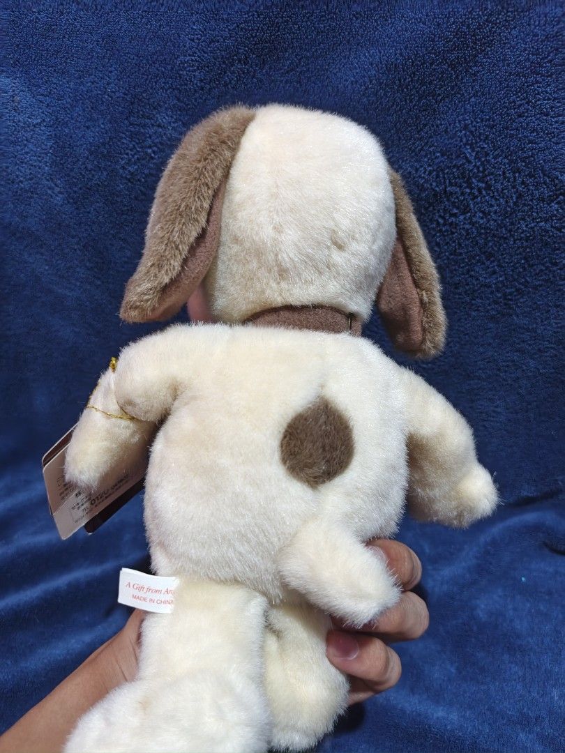 Snoopy plush toy with tag (Category: Plushies & Soft Toys) located in Manila. Submitted by kirstentoyshub (Listing ID 1470379770, Image 3). Description: - Item: Authentic Snoopy plush toy - Color/Design: Soft cream fur with brown ears and a distinctive brown spot on the back - Details: Includes original 'A Gift from Angels' tag with doghouse graphic, attached by a gold string - Condition: Clean fabric, intact stitching, and well-maintained - Orig