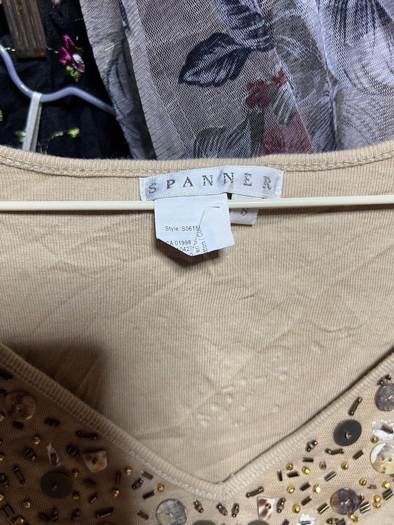 Spanner Beige V-Neck Beaded Top Size S (Category: Blouses) located in Manila. Submitted by threadly (Listing ID 1470399716, Image 3). Description: - Brand: Spanner - Size: Small (Style: S06154) - Color: Beige - Material: Lightweight cotton, relaxed fit - Details: V-neck with wooden beads, sequins, and shell accents - Style: Short sleeves, standard hem, great for casual wear with jeans or skirts.
