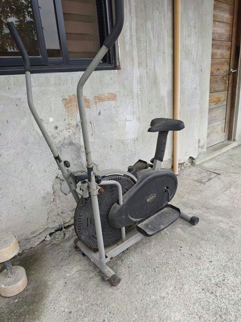 Stationary Exercise Bike with Moving Handlebars (Category: Cardio & Fitness Machines) located in Manila. Submitted by anj2123 (Listing ID 1470365219, Image 1). Description: - Type: Stationary exercise bike for full-body cardio - Design: Dual-action handlebars for upper and lower body workout, padded seat, foot pedals - Color: Grey and black - Build: Heavy, sturdy metal frame - Condition: Used with visible dust, dirt, and surface rust on screws/jo