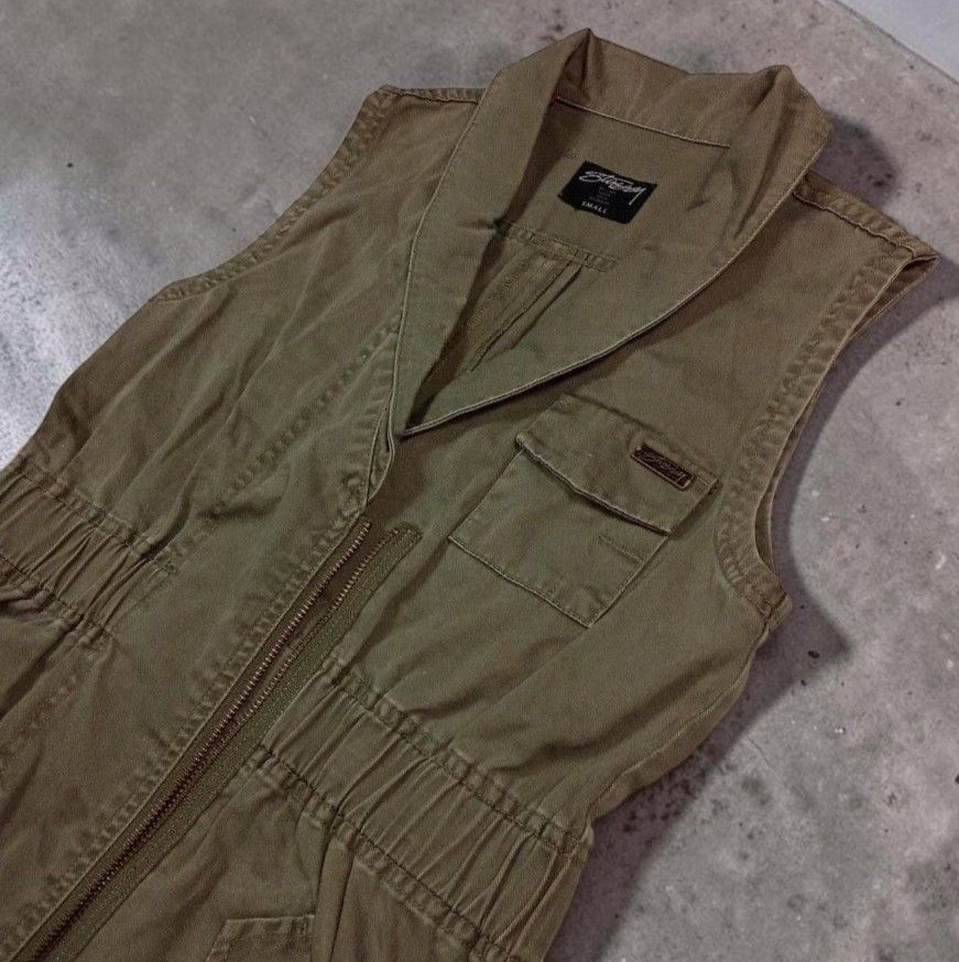Stussy Olive Green Utility Vest (Category: Blouses) located in Manila. Submitted by grmnts_frmthe_slmz (Listing ID 1470391103, Image 3). Description: Olive green Stussy vest, size small. Cotton fabric with a textured vertical weave. Asymmetric front zipper closure and structured collar. Elasticized waist cinches the fit nicely. Multiple utility pockets, including one chest pocket with a metal Stussy logo badge. Curved hem at the back with drawstr