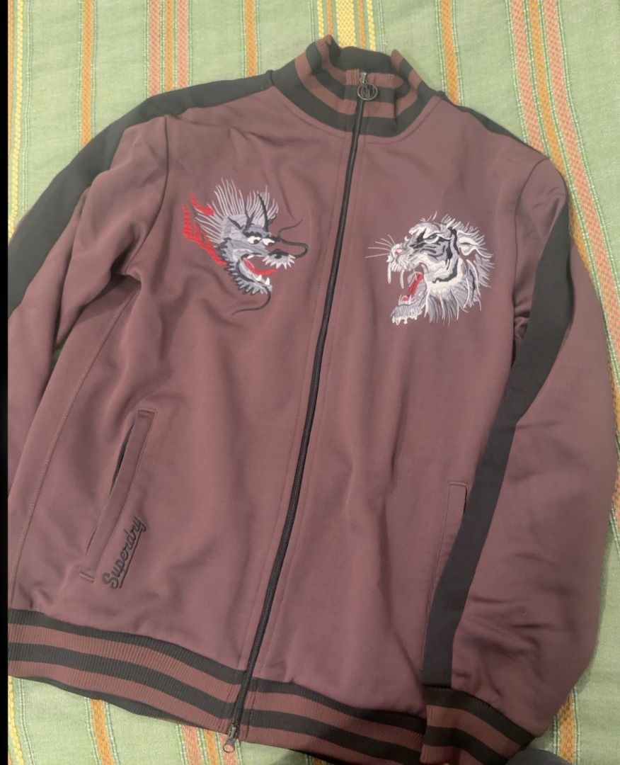 Superdry Vintage Sukajan Jacket (Category: Coats, Jackets and Outerwear) located in Taguig. Submitted by noblephoenix_e3fda3 (Listing ID 1470456462, Image 1). Description: - Color: Brown with contrast dark stripes down the sleeves - Design: Detailed back embroidery featuring a dragon, tiger, mountain scenery, and "Japan" script - Features: Full-zip front, striped ribbed collar, cuffs, and hem - Material: Smooth and sporty fabric, heavyweight - Co
