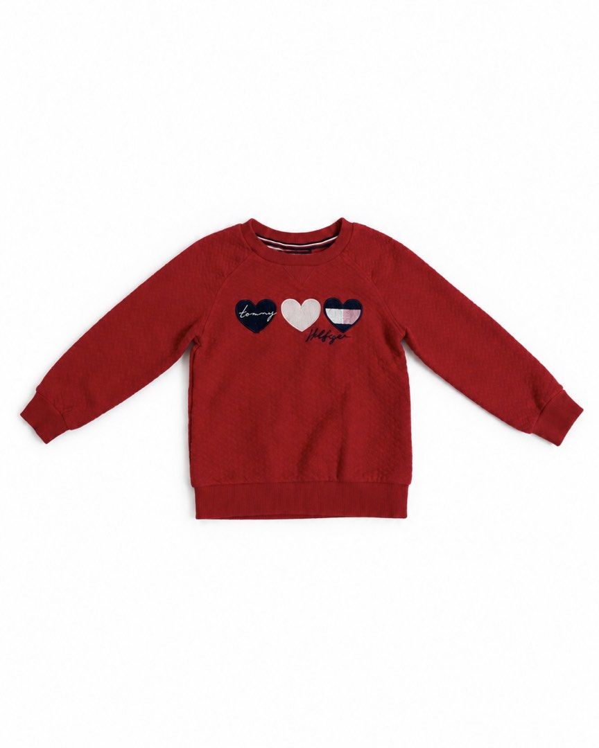 Tommy Hilfiger Red Heart Sweatshirt (Category: Babies & Kids Fashion) located in San Mateo. Submitted by stassiealy (Listing ID 1470498263, Image 1). Description: - Brand: Tommy Hilfiger - Color: Red - Design: Three embroidered hearts with signature branding on the chest - Material: Soft textured knit fabric - Features: Quilted design with ribbed collar, cuffs, and hem - Condition: Excellent pre-loved condition - Perfect for: Casual streetwear an