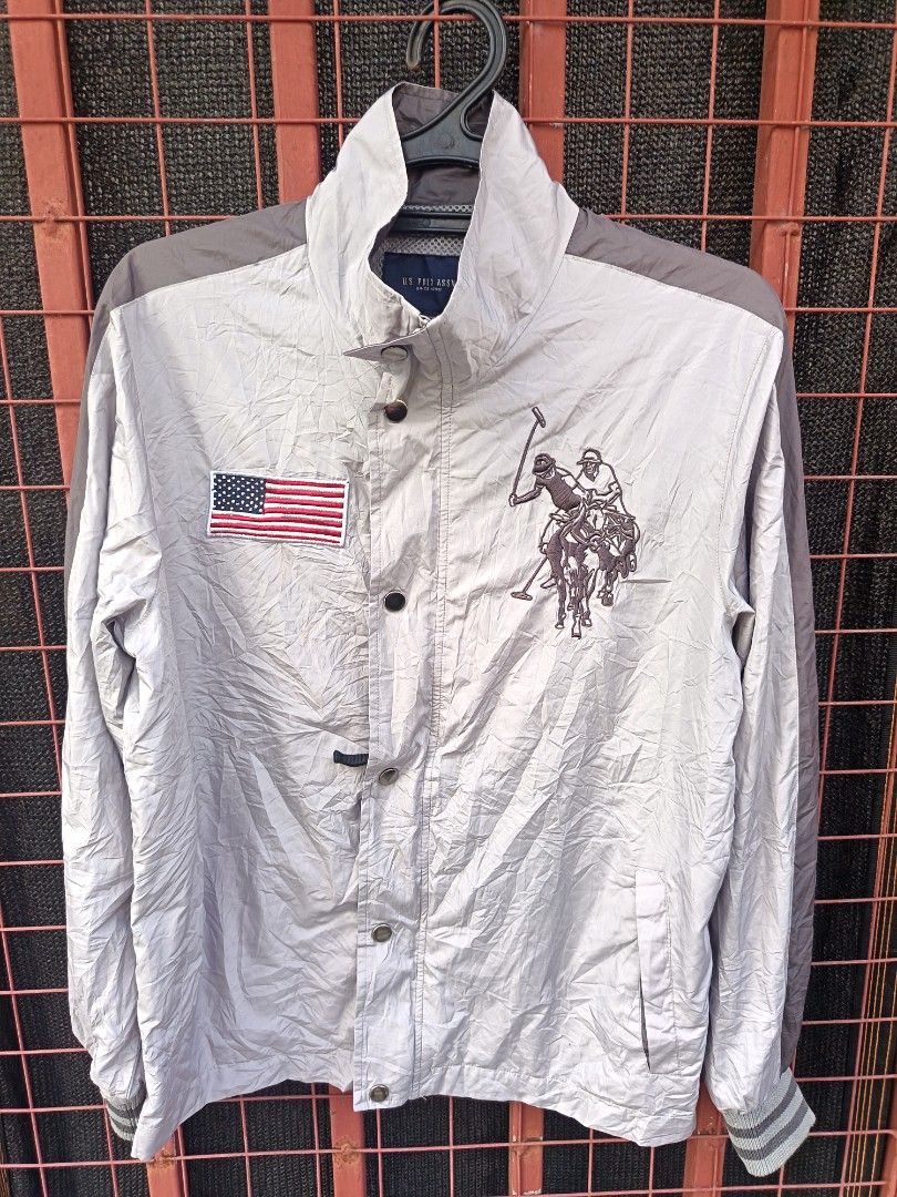 U. S Polo assn (Category: Coats, Jackets and Outerwear) located in Aroroy. Submitted by vin2za06 (Listing ID 1470351190, Image 3). Description: This is a light gray U.S. Polo Assn. windbreaker jacket featuring a large embroidered polo player logo and an American flag patch on the chest..