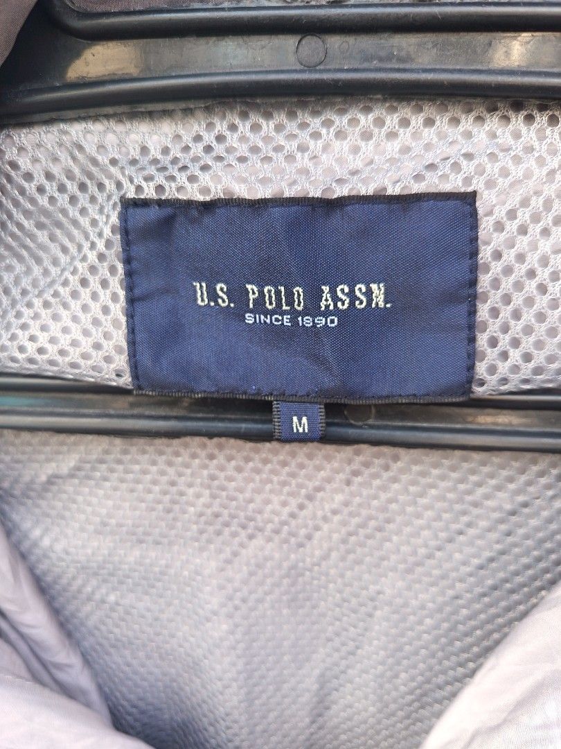 U. S Polo assn (Category: Coats, Jackets and Outerwear) located in Aroroy. Submitted by vin2za06 (Listing ID 1470351190, Image 2). Description: This is a light gray U.S. Polo Assn. windbreaker jacket featuring a large embroidered polo player logo and an American flag patch on the chest..