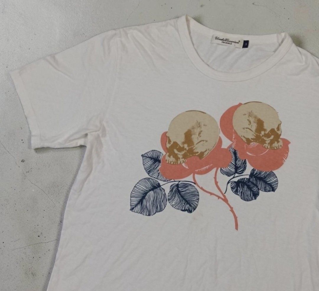Undercoverism S/S 2008 - Skull & Roses - White Tee (Category: Shirts) located in Manila. Submitted by grmnts_frmthe_slmz (Listing ID 1470403850, Image 2). Description: Undercoverism For Rebels graphic tee in white. Front print features two detailed skulls nestled inside pink roses with blue-grey leaves. Tagged size 3. Crew neck and short sleeves. Classic Jun Takahashi aesthetic. Minor natural wear on fabric, print remains crisp. Undercoverism S/S