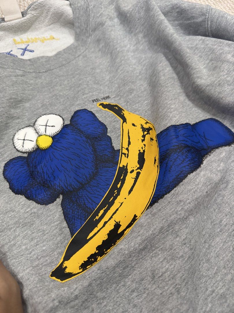 Uniqlo x Kaws + Warhol Grey Sweatshirt (Category: Coats, Jackets and Outerwear) located in Valenzuela. Submitted by crabncorn (Listing ID 1470364024, Image 2). Description: - Brand: Uniqlo UT x Kaws + Warhol - Color: Heather Grey - Size: XL - Design: Blue character graphic and yellow banana print with "PEEL HERE" detail on front - Back Details: Embroidered blue XX and yellow Andy Warhol signature on collar - Condition: Excellent / Brand new with 
