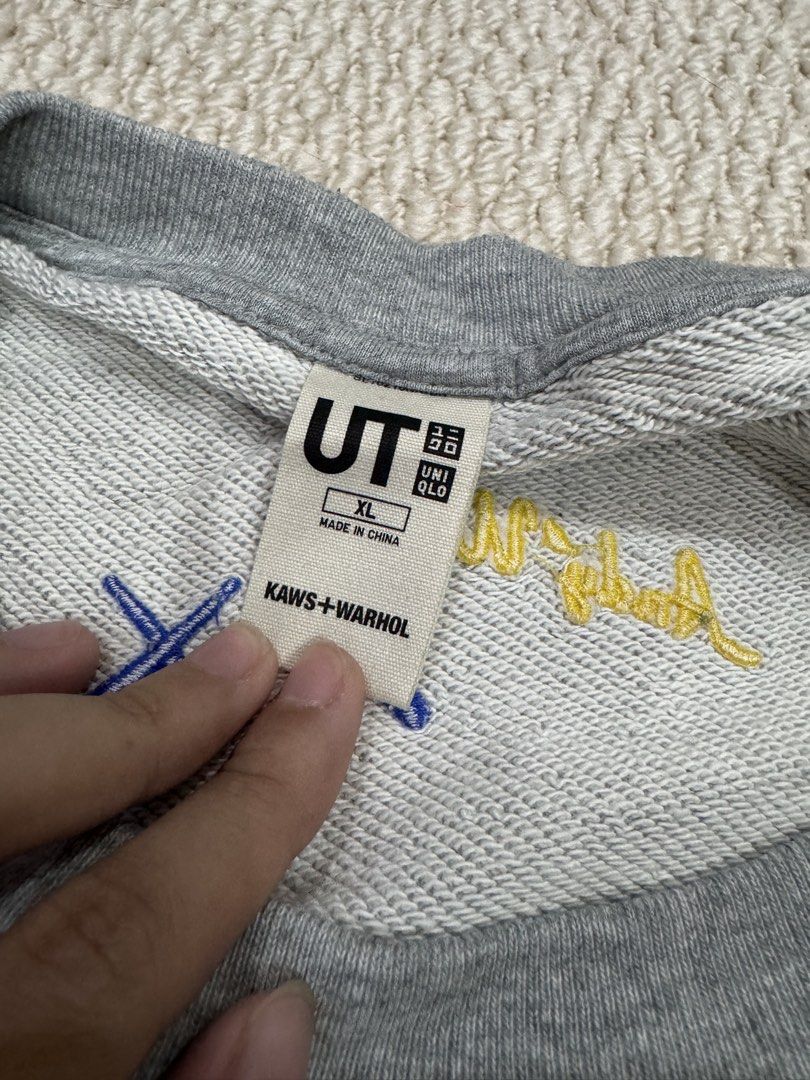 Uniqlo x Kaws + Warhol Grey Sweatshirt (Category: Coats, Jackets and Outerwear) located in Valenzuela. Submitted by crabncorn (Listing ID 1470364024, Image 3). Description: - Brand: Uniqlo UT x Kaws + Warhol - Color: Heather Grey - Size: XL - Design: Blue character graphic and yellow banana print with "PEEL HERE" detail on front - Back Details: Embroidered blue XX and yellow Andy Warhol signature on collar - Condition: Excellent / Brand new with 