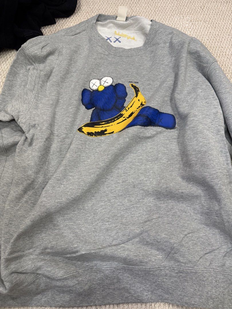 Uniqlo x Kaws + Warhol Grey Sweatshirt (Category: Coats, Jackets and Outerwear) located in Valenzuela. Submitted by crabncorn (Listing ID 1470364024, Image 1). Description: - Brand: Uniqlo UT x Kaws + Warhol - Color: Heather Grey - Size: XL - Design: Blue character graphic and yellow banana print with "PEEL HERE" detail on front - Back Details: Embroidered blue XX and yellow Andy Warhol signature on collar - Condition: Excellent / Brand new with 