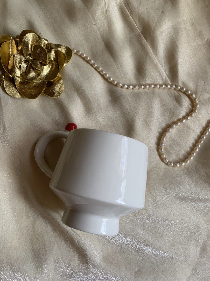 White ceramic mug with red ball detail (Category: Coffee & Tea Tableware) located in Daraga. Submitted by shevvv28 (Listing ID 1470457893, Image 1). Description: - Color/Material: White ceramic with smooth glazed finish - Design: Footed base and unique handle with a bright red round bead - Condition: Excellent, clean interior and exterior with no chips or cracks - Use: Great minimal piece for morning coffee or desk use.