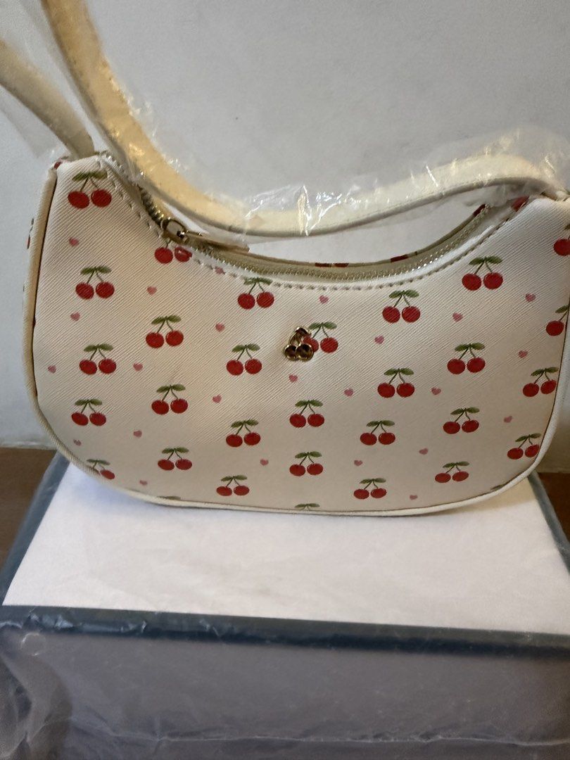 White Cherry Print Shoulder Bag (Category: Shoulder Bags) located in Bulacan. Submitted by emjay_17 (Listing ID 1470426680, Image 1). Description: - Style: White shoulder bag with red cherry and tiny pink heart all-over print - Condition: Brand new, never used, with plastic wrapping still on the strap - Dimensions: Roughly 20cm (across) x 15cm (down) - Hardware & Closure: Secure top zipper closure with gold-tone hardware - Storage: Comes stuffed 