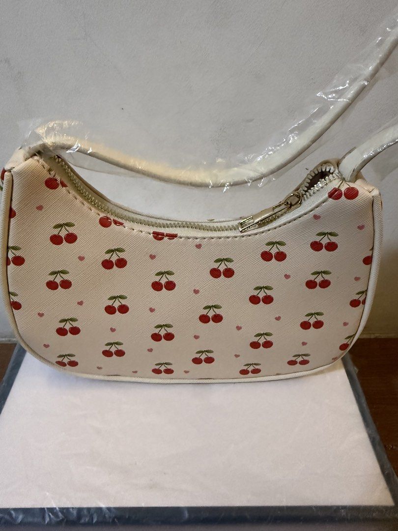 White Cherry Print Shoulder Bag (Category: Shoulder Bags) located in Bulacan. Submitted by emjay_17 (Listing ID 1470426680, Image 2). Description: - Style: White shoulder bag with red cherry and tiny pink heart all-over print - Condition: Brand new, never used, with plastic wrapping still on the strap - Dimensions: Roughly 20cm (across) x 15cm (down) - Hardware & Closure: Secure top zipper closure with gold-tone hardware - Storage: Comes stuffed 
