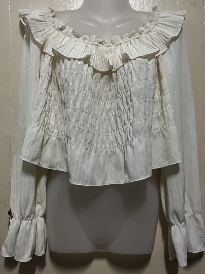 White off-shoulder ruffled smocked long sleeve blouse (Category: Blouses) located in Tabuk. Submitted by zenwolf-1867 (Listing ID 1470531967, Image 1). Description: - Color: White - Style: Off-shoulder, romantic, cropped - Fit: Stretchy smocked torso for a flattering silhouette - Details: Ruffle collar and cuffs with sheer long sleeves - Fabric: Super lightweight and textured - Styling: Great for pairing with high-waisted jeans or skirts.