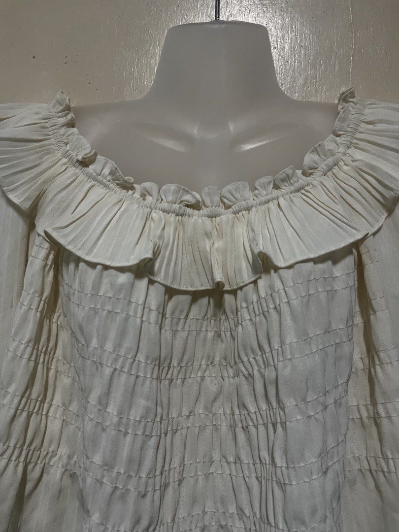 White off-shoulder ruffled smocked long sleeve blouse (Category: Blouses) located in Tabuk. Submitted by zenwolf-1867 (Listing ID 1470531967, Image 2). Description: - Color: White - Style: Off-shoulder, romantic, cropped - Fit: Stretchy smocked torso for a flattering silhouette - Details: Ruffle collar and cuffs with sheer long sleeves - Fabric: Super lightweight and textured - Styling: Great for pairing with high-waisted jeans or skirts.