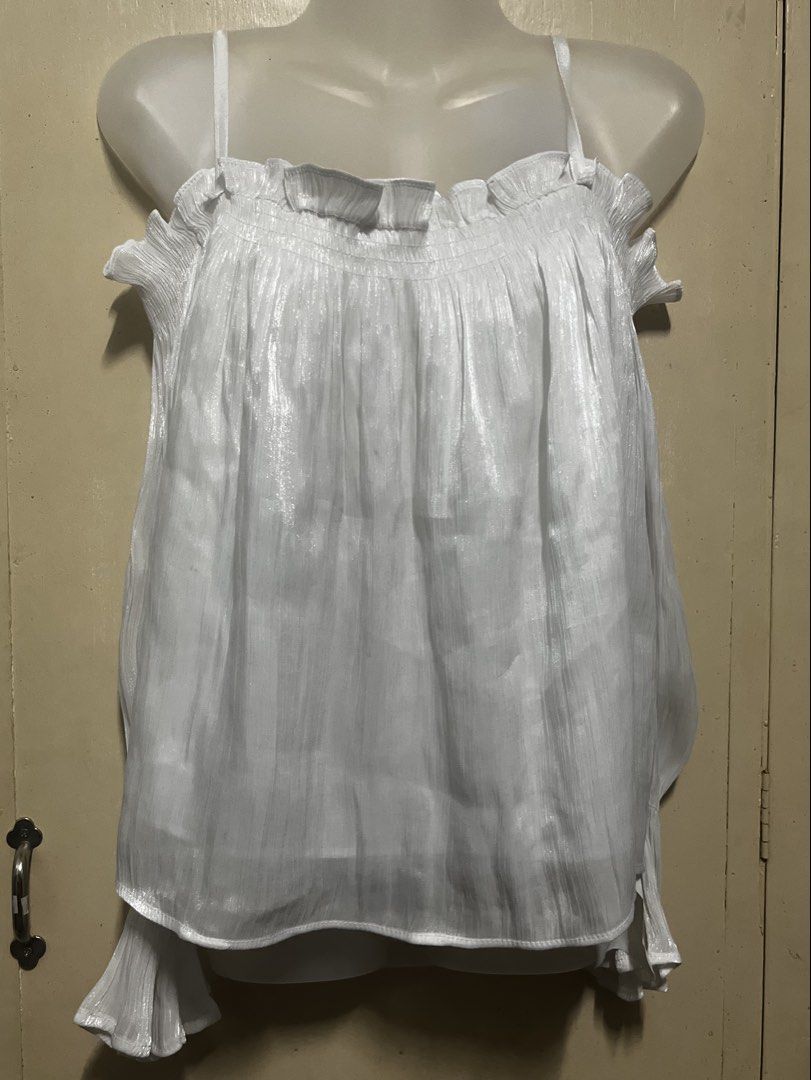 White Pleated Cami Top with Ruffle Details (Category: Sleeveless) located in Tabuk. Submitted by zenwolf-1867 (Listing ID 1470532233, Image 2). Description: - Color: White - Style: Sleeveless cami top with thin spaghetti straps - Material: Lightweight, shiny, and textured pleated fabric - Design details: Ruffled neckline and stylish flowy fit with extra draped side panels - Perfect for layering or casual sunny days!.