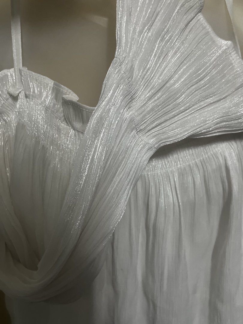 White Pleated Cami Top with Ruffle Details (Category: Sleeveless) located in Tabuk. Submitted by zenwolf-1867 (Listing ID 1470532233, Image 3). Description: - Color: White - Style: Sleeveless cami top with thin spaghetti straps - Material: Lightweight, shiny, and textured pleated fabric - Design details: Ruffled neckline and stylish flowy fit with extra draped side panels - Perfect for layering or casual sunny days!.