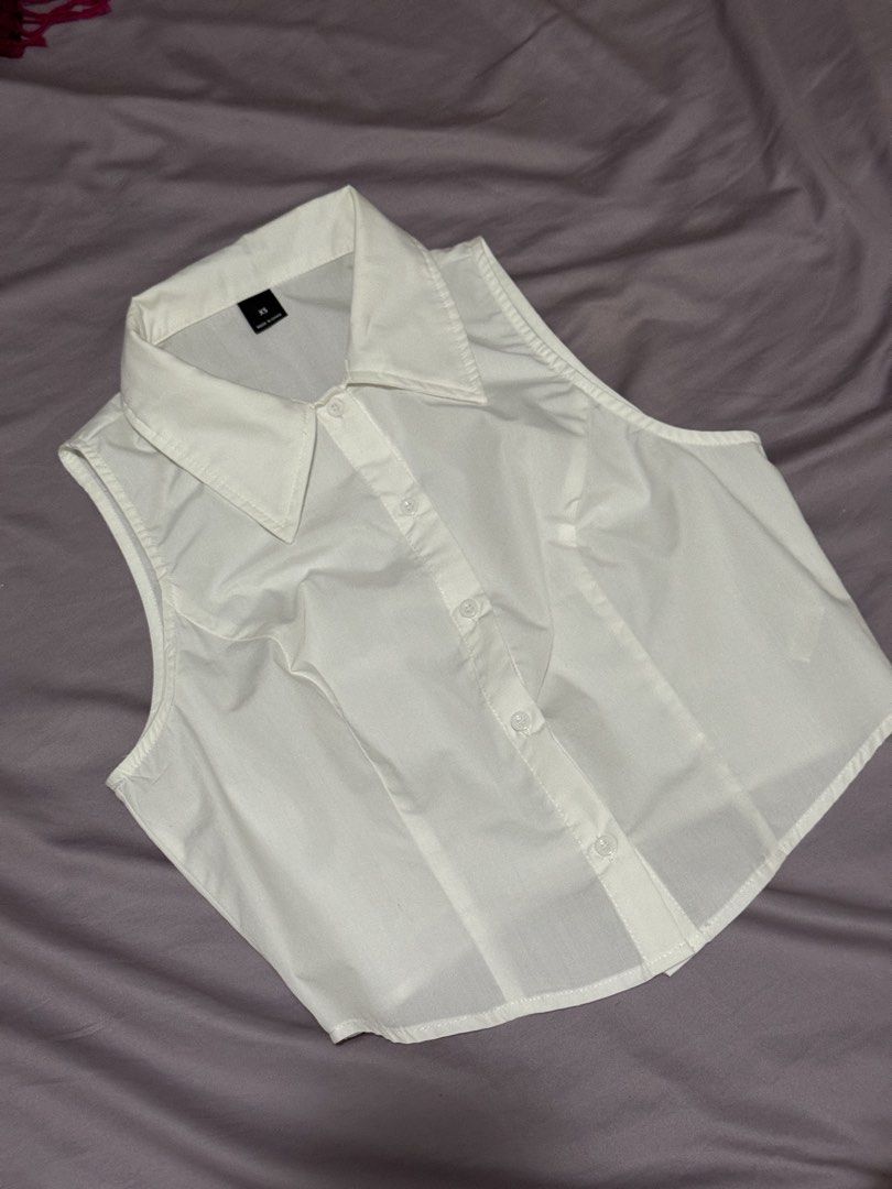 White sleeveless collared crop button down shirt top (Category: Blouses) located in Angeles City. Submitted by m1lkramen (Listing ID 1470464226, Image 1). Description: - Color: White - Size: XS (tagged inside collar) - Style: Sleeveless, cropped, collared top with front button closure - Fit: Tailored through the body with structured lapels - Condition: Clean fabric, great basic for layering or standalone wear · · ─ ·✶· ─ · · length: 15.5 in width