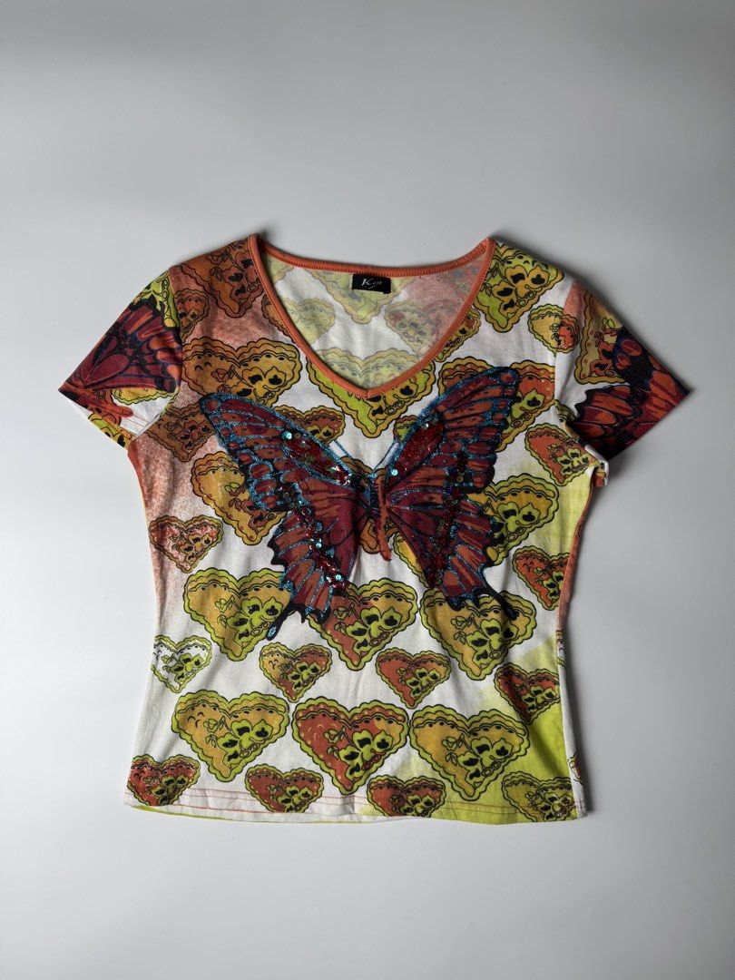 Y2K Butterfly Sequin Graphic V-Neck Tee (Category: Shirts) located in Manila. Submitted by babygirly2k (Listing ID 1470403223, Image 1). Description: - Style: Y2K short-sleeve top - Design: White base with all-over colorful heart and butterfly pattern - Details: Large embroidered front butterfly with blue glitter edging and red sequins - Trim: Orange ribbed V-neckline - Branding: 'Ken' label on inside collar - Measurements: 17" pit-to-pit, 22" le