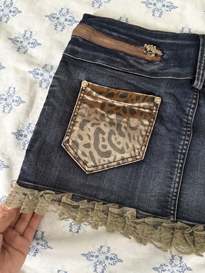 Y2K Leopard Denim Ruffle Mini Skirt Size M (Category: Skirts) located in Angeles City. Submitted by charishurb08031 (Listing ID 1470430170, Image 3). Description: - Size: 29-30 (with inner drawstring waistband) Length: 12 - Design: Dark wash denim with brown leopard print panels and rhinestone front graphic - Details: Decorative zippers and functional back pockets - Hem: Cute light brown lace ruffle trim.