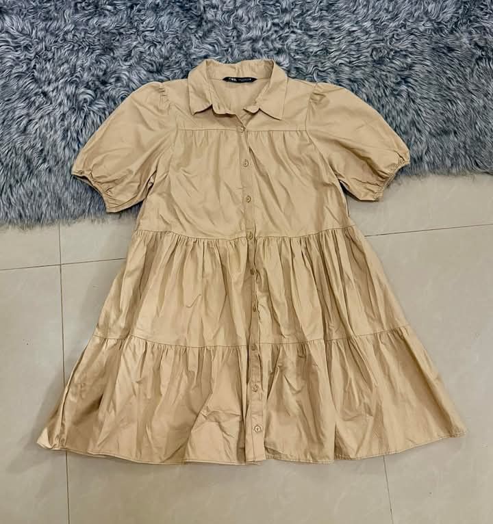 Zara Button-Up Paperdoll Dress (Category: Dresses) located in Roxas City. Submitted by secondasnew_ph (Listing ID 1470532506, Image 1). Description: - Brand/Item: Zara Tiered Shirt Dress - Color: Beige - Can fit to S-Medium body frame - Size: Refer to collar tag photo - Features: Short puff sleeves, collared neckline, button-down front - Style: Knee-length with a flared, multi-tier skirt - Condition: Clean fabric, structured fit - Versatility: Gr